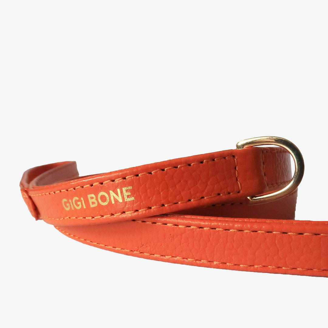 Correa de perro en piel color rojo naranja con mosquetón y argolla dorada.  Marca GiGi BONE impresa en el cuero en letras doradas a juego con los herrajes. Piel italiana de curtido vegetal y herrajes de gran calidad. Hecho a mano, con bordes de piel doblada y cosida, sin recubrimientos plásticos, lo que le da una estética premium y gran durabilidad