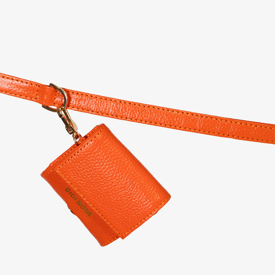 Portabolsas higiénicas de piel color rojo naranja. Logo GiGi BONE impreso en el cuero en letras doradas a juego con los herrajes Ojal de metal dorado en la parte baja para facilitar la dispensa de bolsas Hecho a mano con piel italiana de curtido vegetal